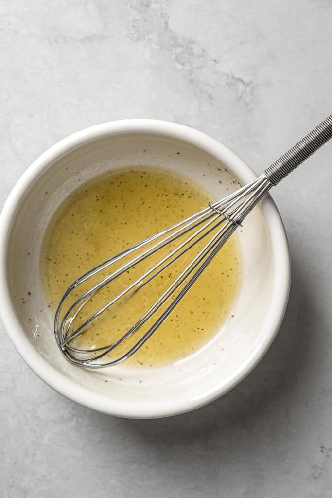 A bowl with lime juice, olive oil, pepper, and a whisk