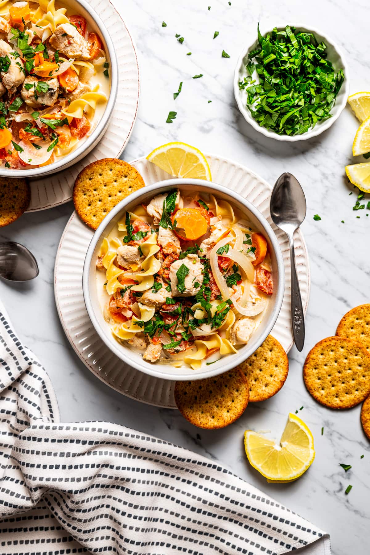 Creamy chicken pasta served in two bowls, with crackers and lemons arranged around the bowls.
