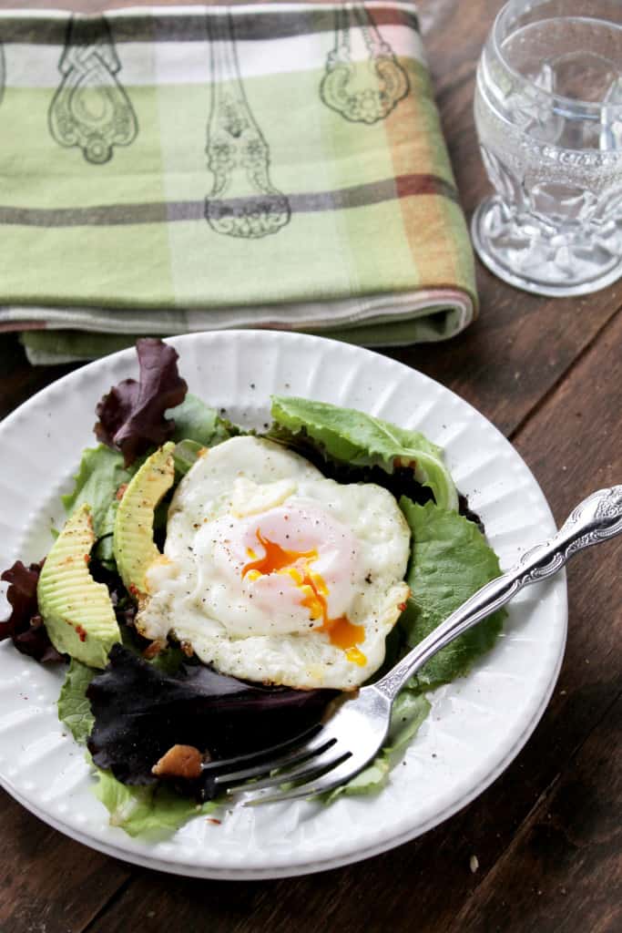 A healthy salad with avocado and egg on top in a white plate with a fork