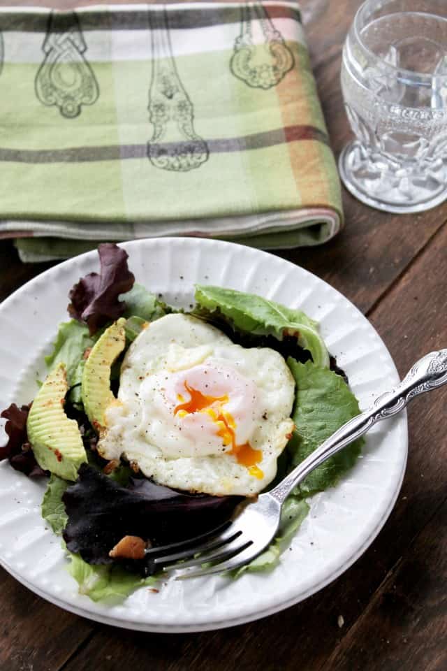 A white plate filled with salad, avocado and topped with a fried egg.