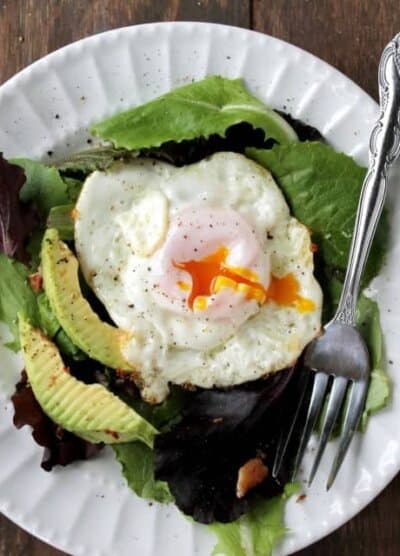 A white plate filled with lettuce, avocado and topped with a fried egg