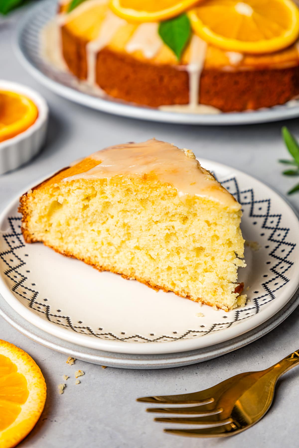 Slice of orange cake served on a white plate, with the full cake set in the background.
