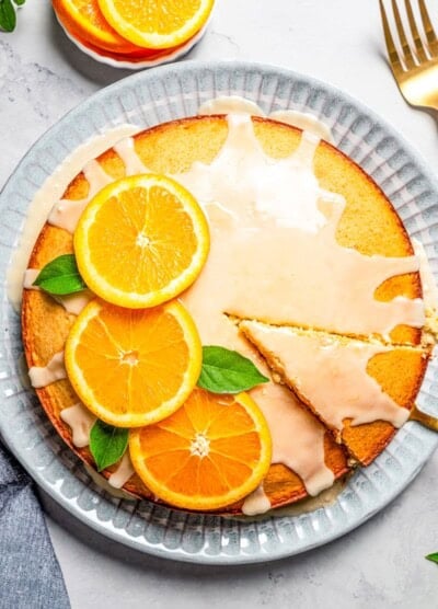 Overhead view of a glazed olive oil cake garnished with orange slices and mint leaves.
