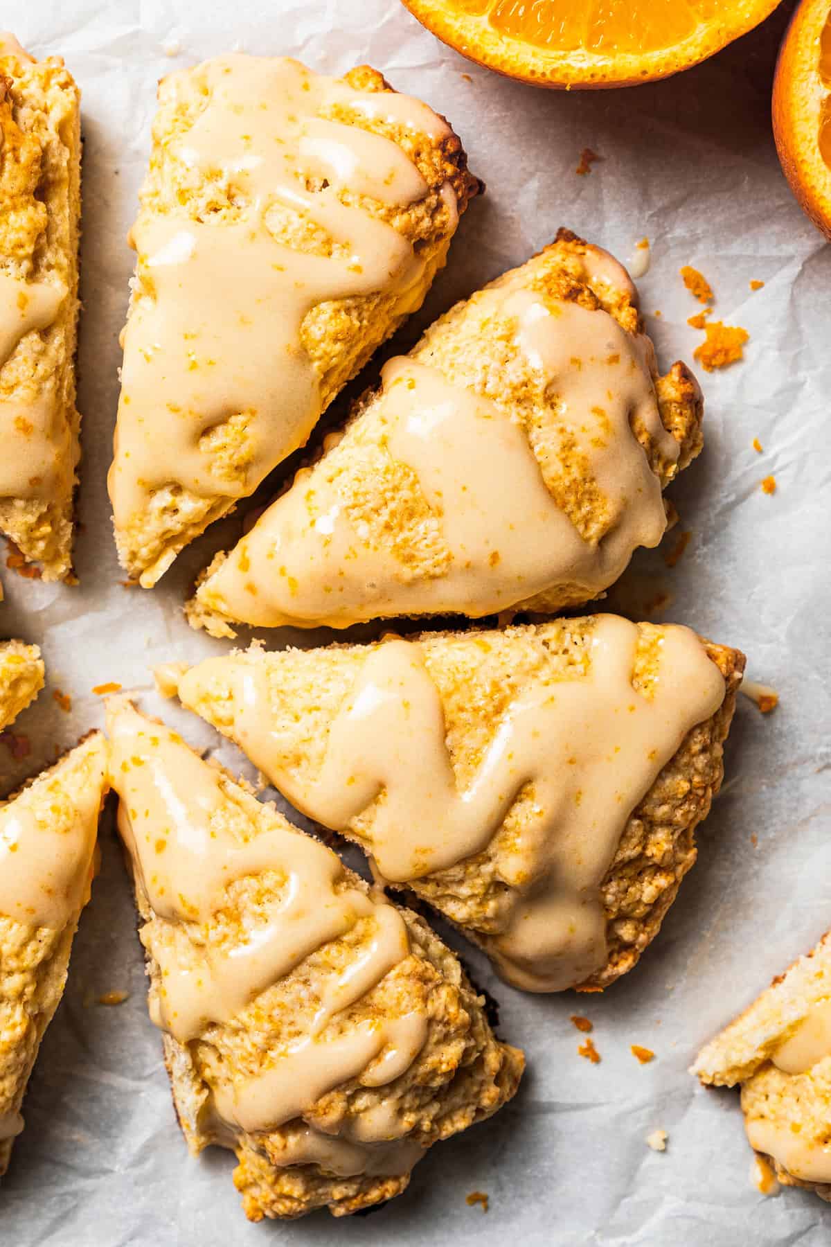 Vanilla orange scones drizzled with a glaze and set next to halved oranges.