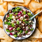 Overhead view of a bowl of corn salsa with a spoon in it, surrounded by wonton chips..