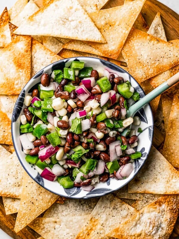 Overhead view of a bowl of corn salsa with a spoon in it, surrounded by wonton chips..