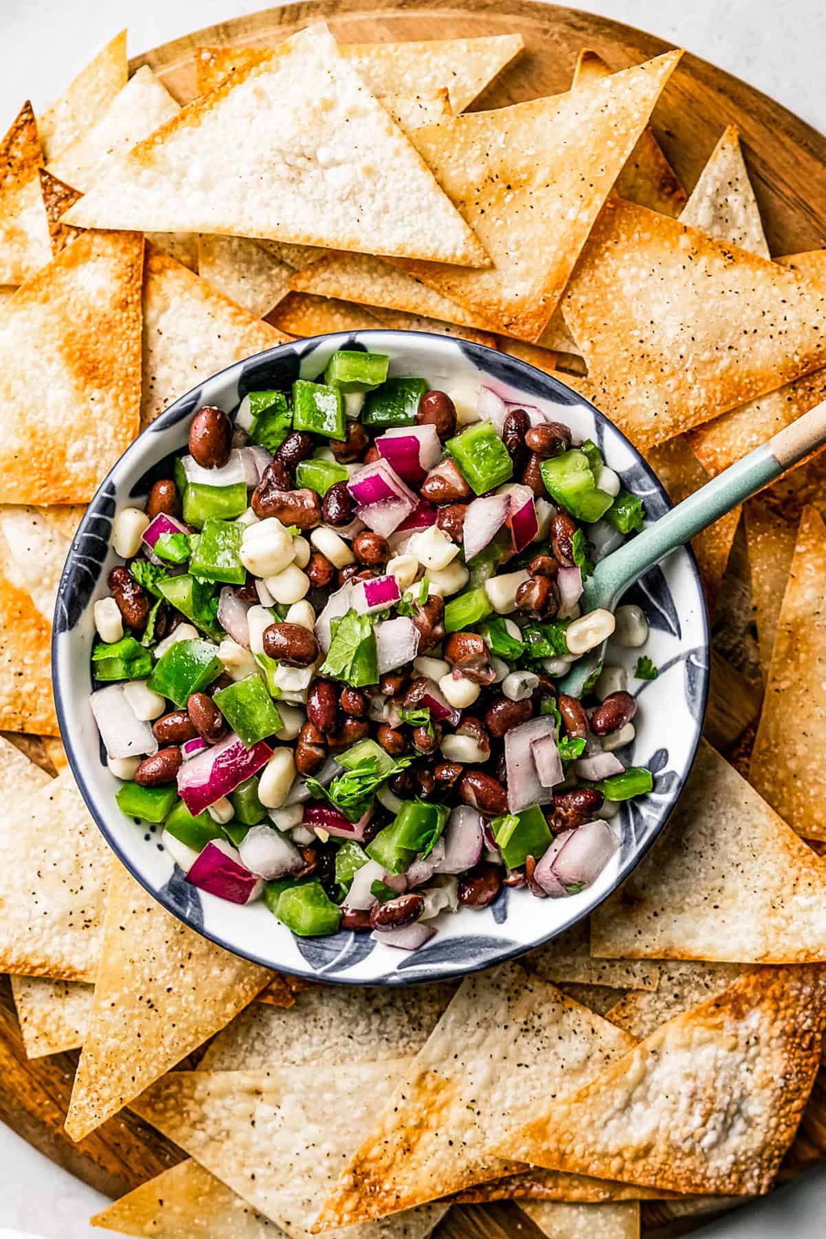 Overhead view of a bowl of corn salsa with a spoon in it, surrounded by wonton chips..