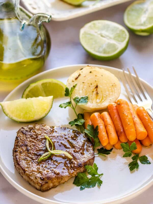 Steak and veggies on a white plate with lime wedges.