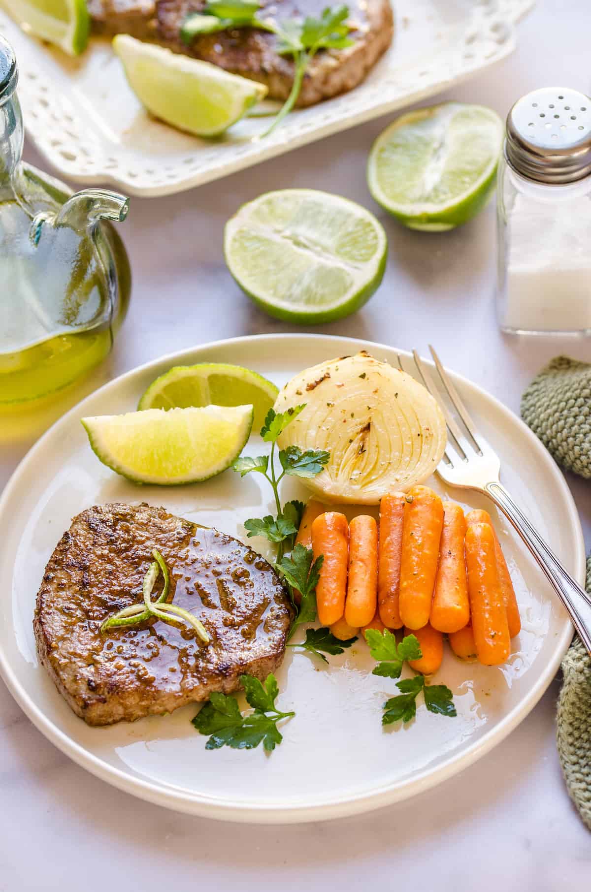 A serving of steak, carrots, and onions on a dinner plate with lime wedges.
