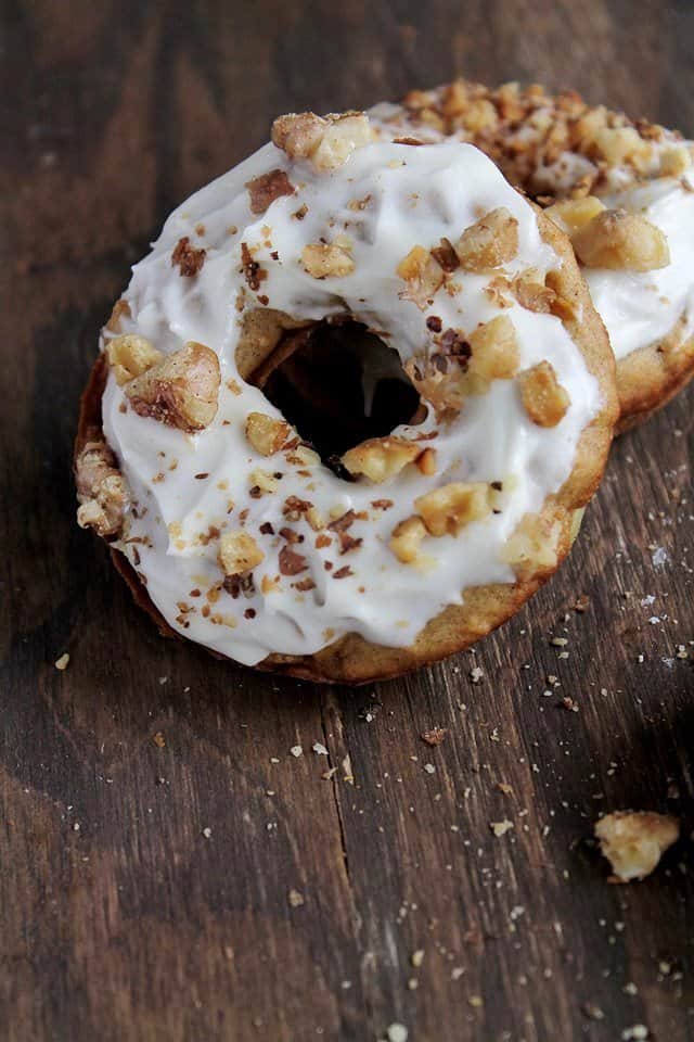 Two Baked Carrot Cake Doughnuts on a wooden table.