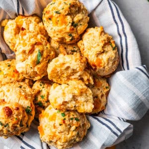 Cheddar bay biscuits piled in a serving bowl lined with a striped dishcloth.