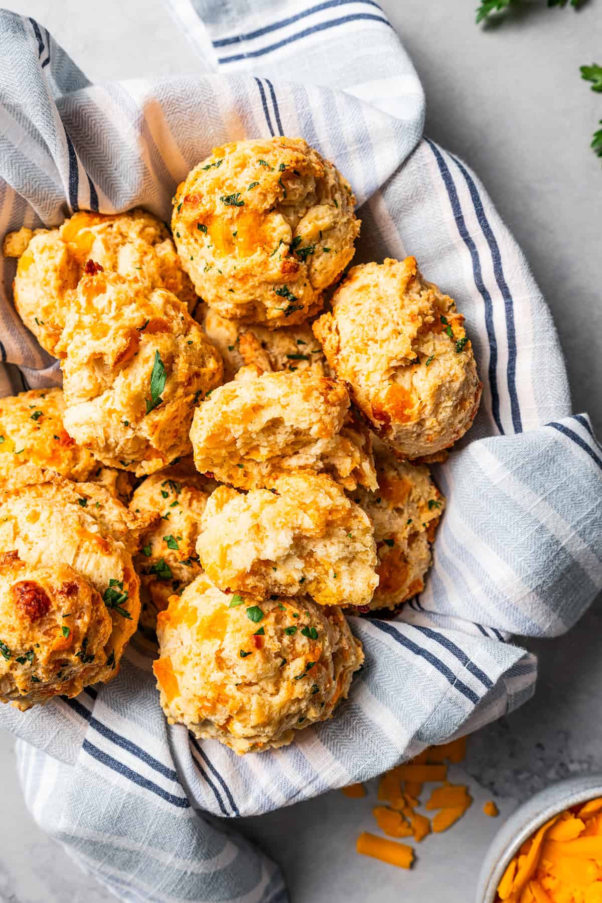 Cheddar bay biscuits piled in a serving bowl lined with a striped dishcloth.