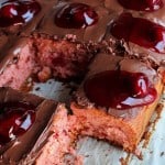 A cake covered in chocolate frosting and cherry pie filling with two missing slices