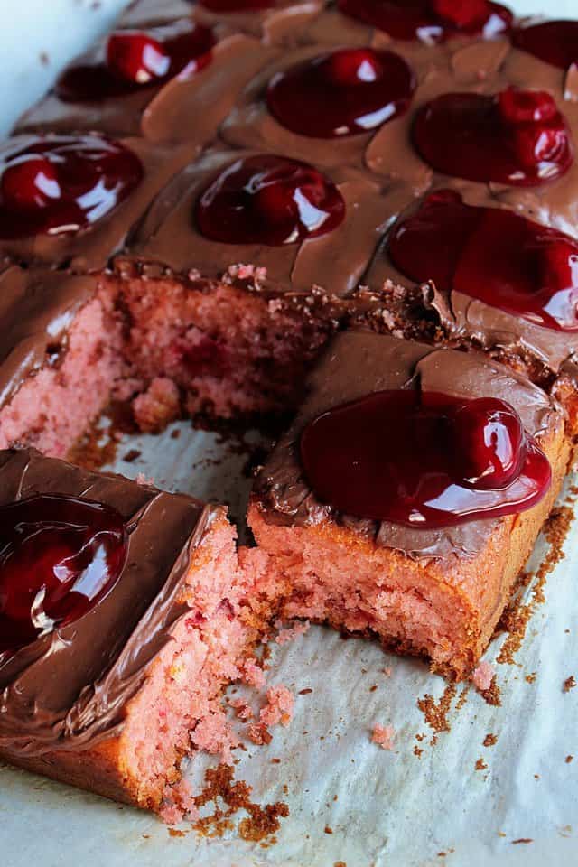 A cake covered in chocolate frosting and cherry pie filling with two missing slices