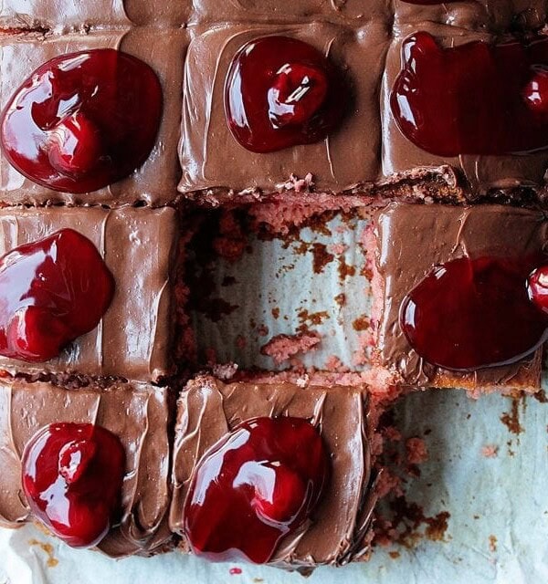 Overhead view of chocolate cherry cake cut into slices, topped with dollops of cherry pie filling, with one slice missing.