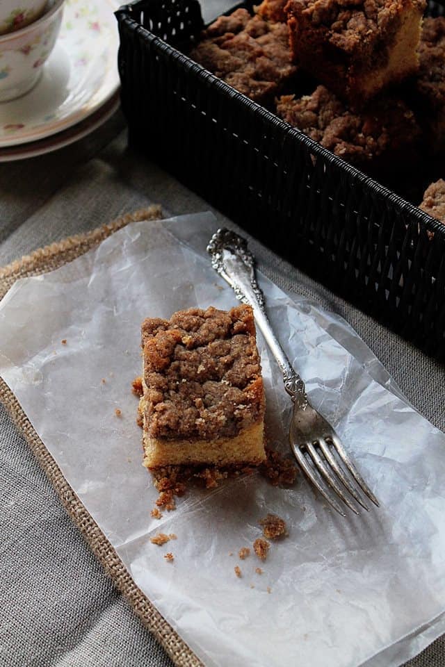 A single slice of New York Crumb Cake on a napkin next to a basket filled with more slices.