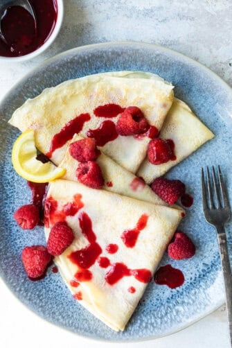 Crepes with raspberries and a lemon wedge.