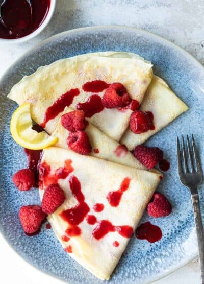 Crepes with raspberries and a lemon wedge.