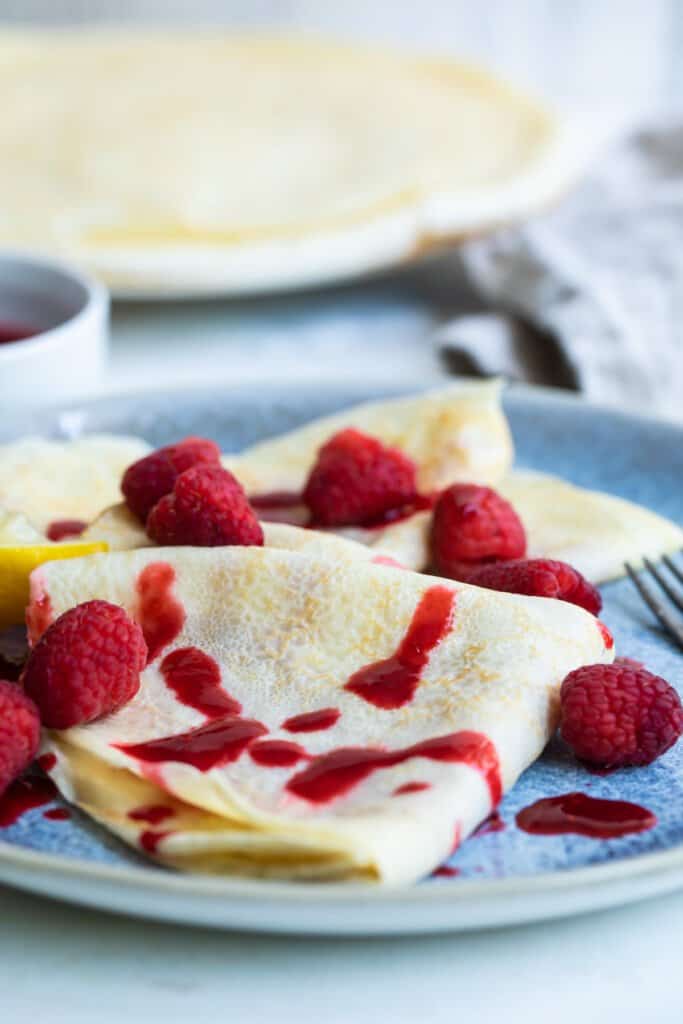 Lemon crepes with raspberry sauce on a plate.