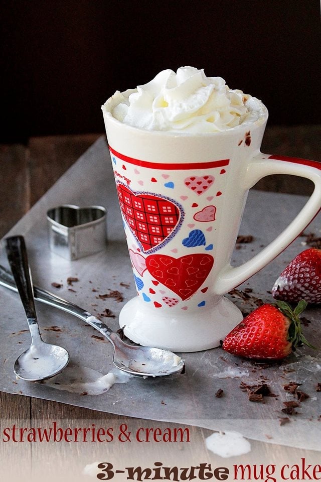 A mug filled with cake and whipped cream on a tray next to two whole strawberries.