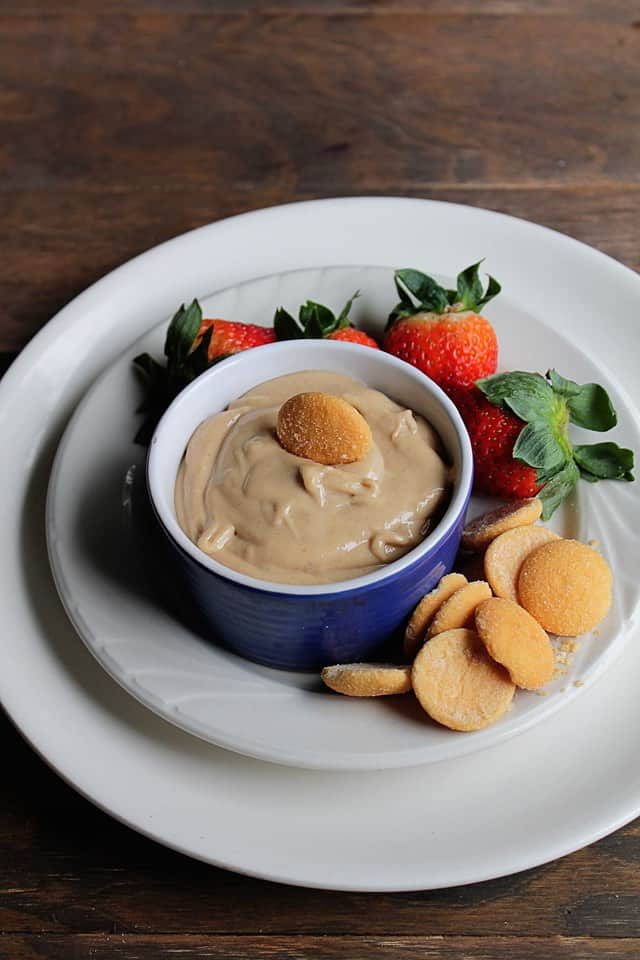 Peanut Butter and Banana Dip served in a small blue bowl surrounded by strawberries and vanilla wafers.