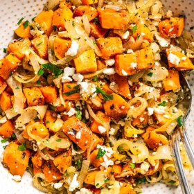 Diced and baked sweet potatoes served in a bowl with onions, herbs, and feta cheese.