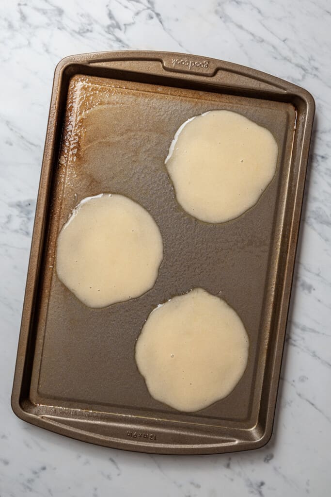 Three circles of raw cannoli dough on a baking sheet