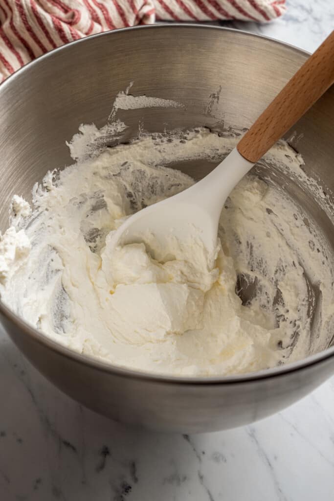 A mixing bowl with whipped cream and a spatula