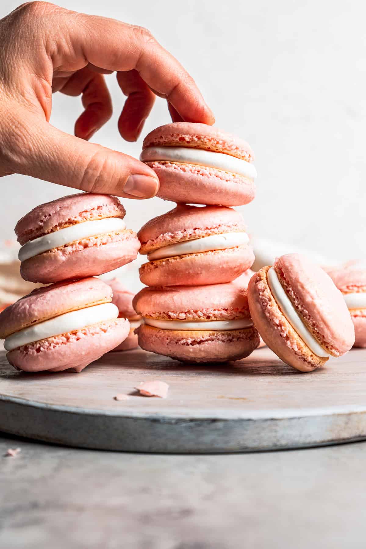 A hand picking up a macaron from a stack of French macarons.