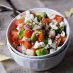 Sliced avocado in a bowl with crumbled feta cheese and diced tomatoes and onions.