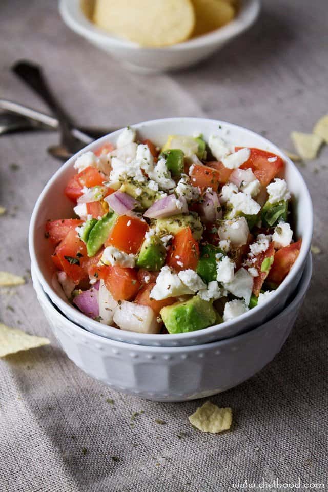 Sliced avocado in a bowl with crumbled feta cheese and diced tomatoes and onions.