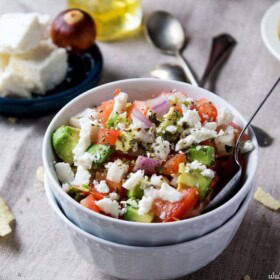 A ramekin filled with fresh avocado salsa in front of a dish filled with chips and another filled with feta cheese.