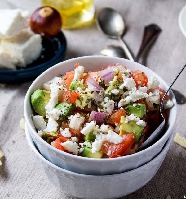 A ramekin filled with fresh avocado salsa in front of a dish filled with chips and another filled with feta cheese.