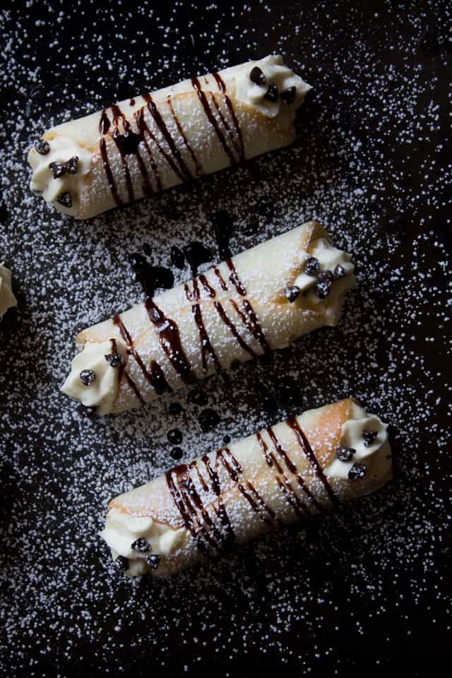 A top view of three cannolis with a dusting of powdered sugar and chocolate drizzled over the tops