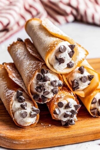 Six cannolis forming a pyramid on a cutting board with a kitchen towel in the background.