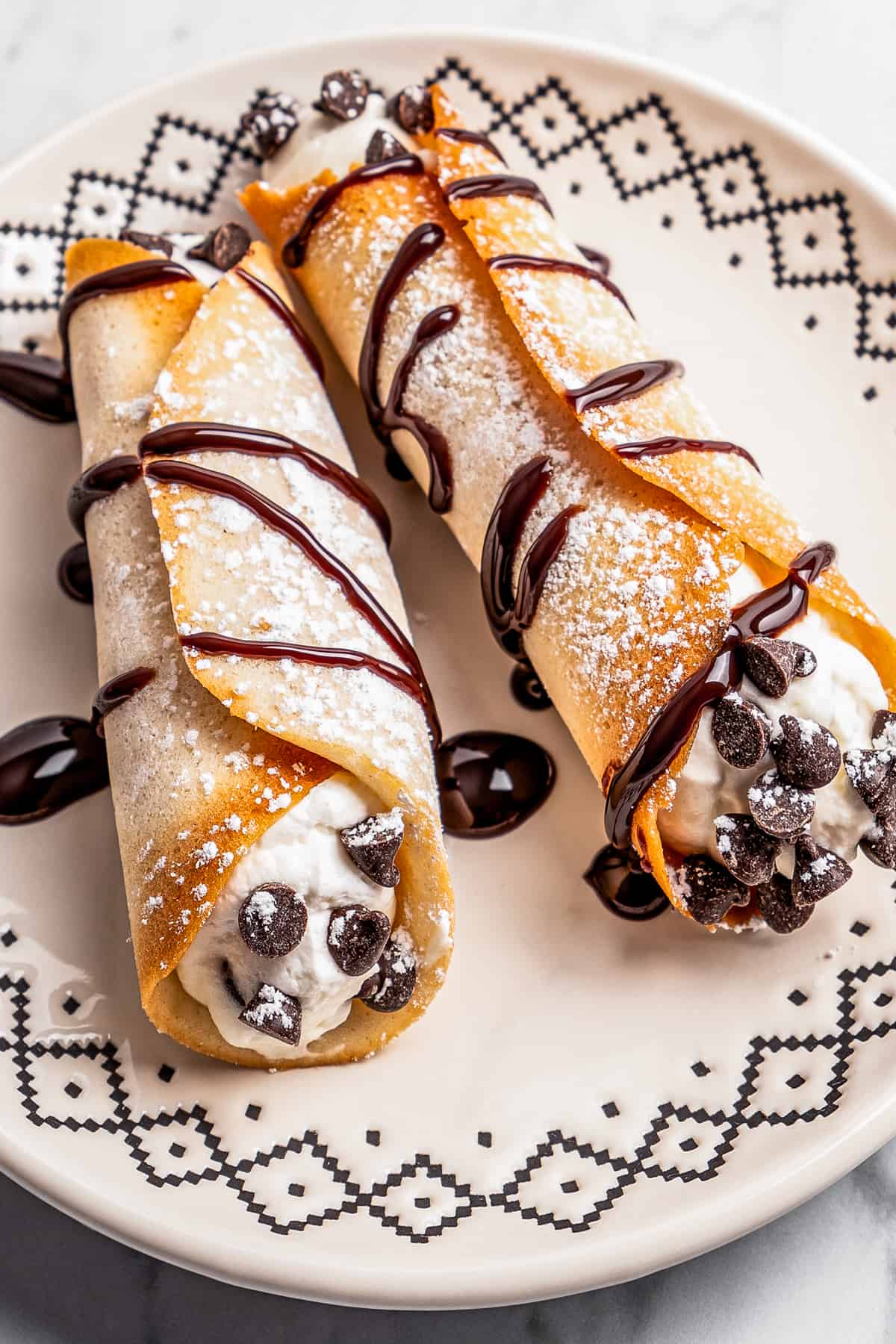 Two cannolis on a plate with chocolate drizzled on top.