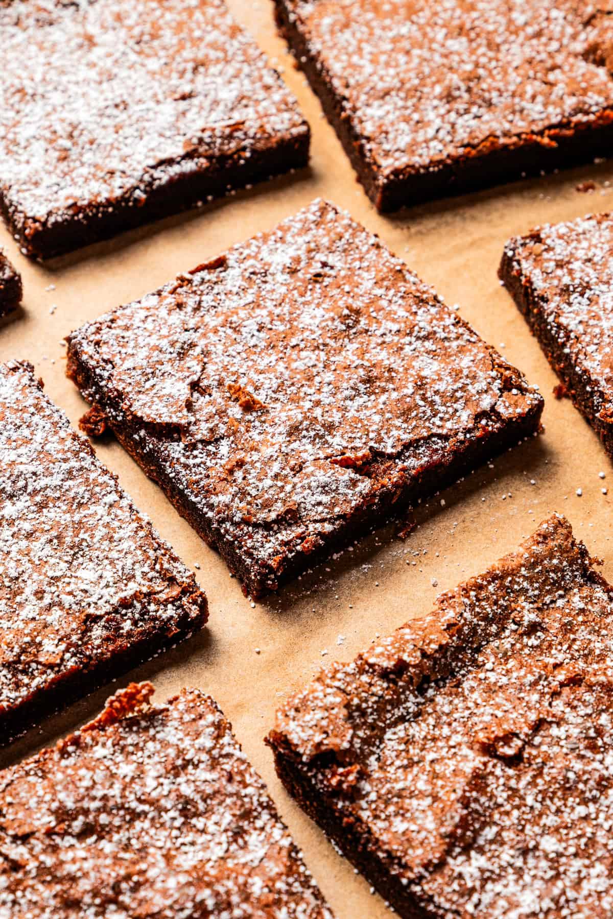 Make fudgy Nutella brownies by whipping eggs and adding Nutella. That's it! These brownies are extra chocolatey and naturally gluten-free. Nutella brownies arranged on parchment paper and dusted with powdered sugar.