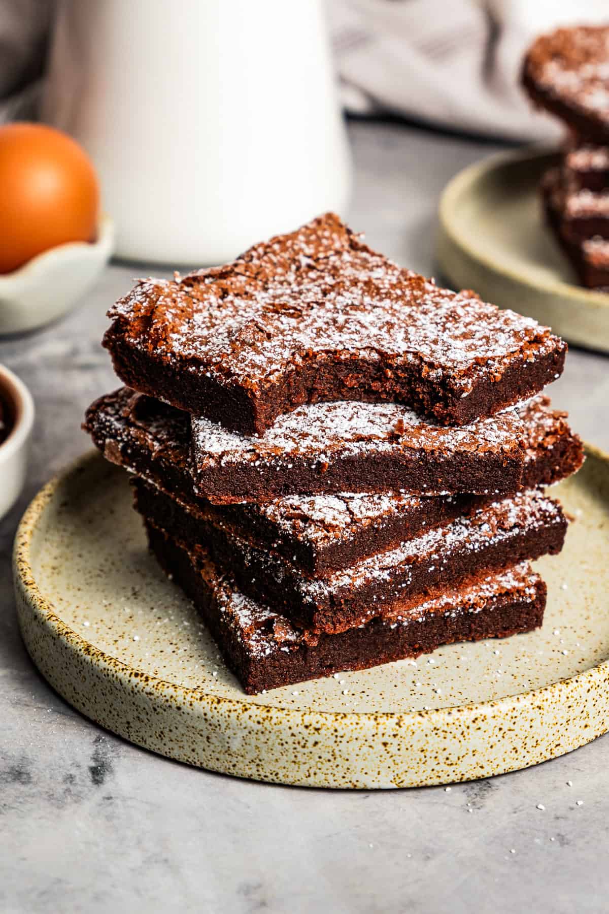 Make fudgy Nutella brownies by whipping eggs and adding Nutella. That's it! These brownies are extra chocolatey and naturally gluten-free. A stack of Nutella brownies on a stoneware plate, with a bite missing from the top brownie.