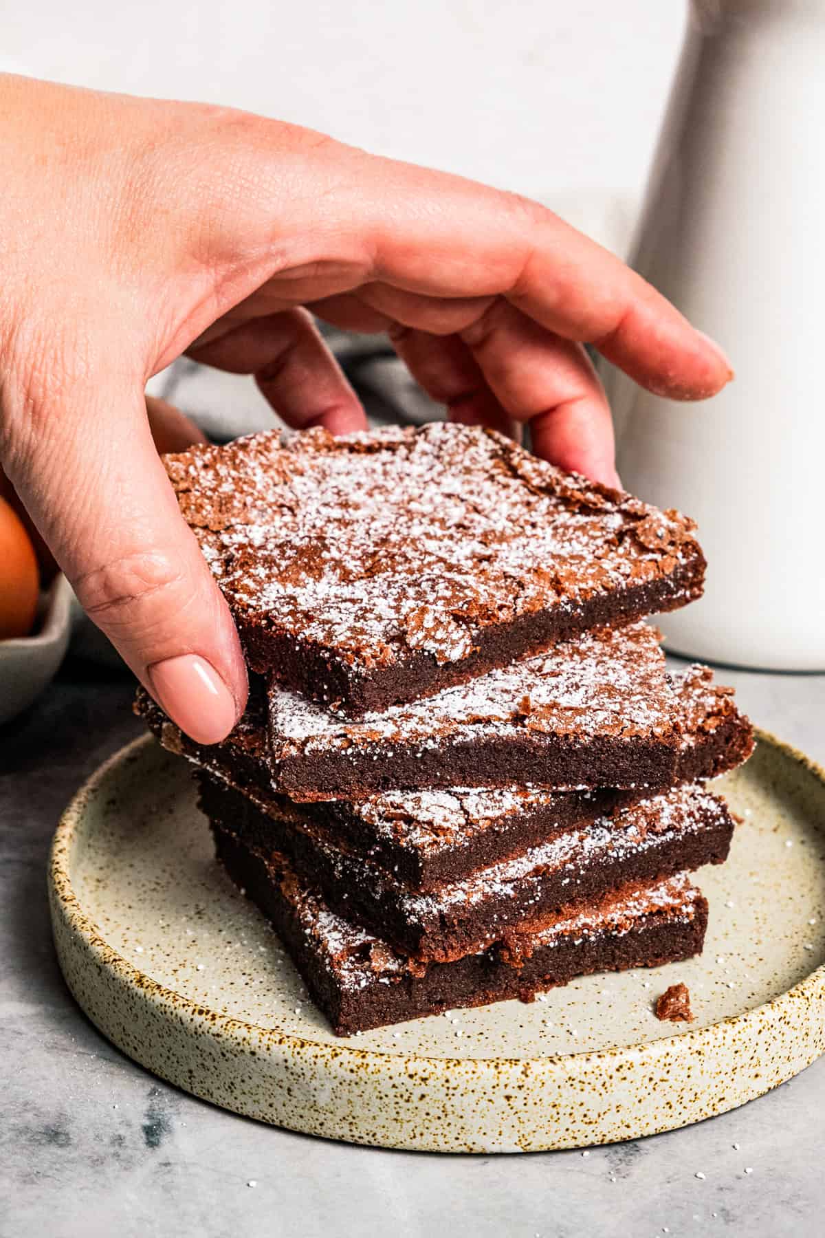 Make fudgy Nutella brownies by whipping eggs and adding Nutella. That's it! These brownies are extra chocolatey and naturally gluten-free. A hand lifting the top brownie from a stack of several.