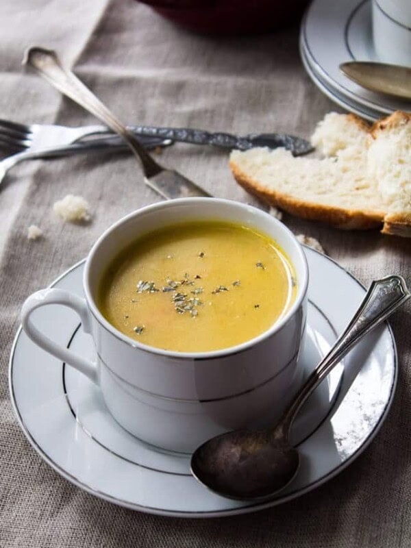 Serving bowl of creamy parsnip potato soup with a slice of bread in the background.