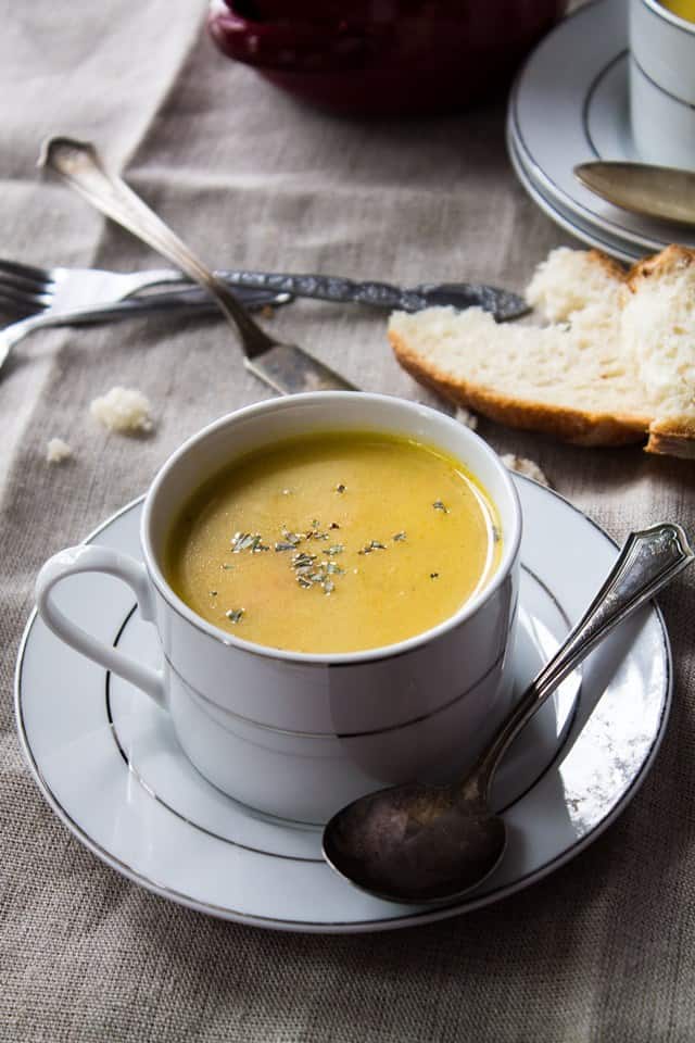 Serving bowl of creamy parsnip potato soup with a slice of bread in the background.