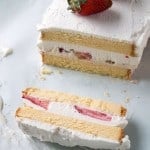 A single slice of Strawberries and Cream Ice Cream Cake lying on its side next to the rest of the cake.