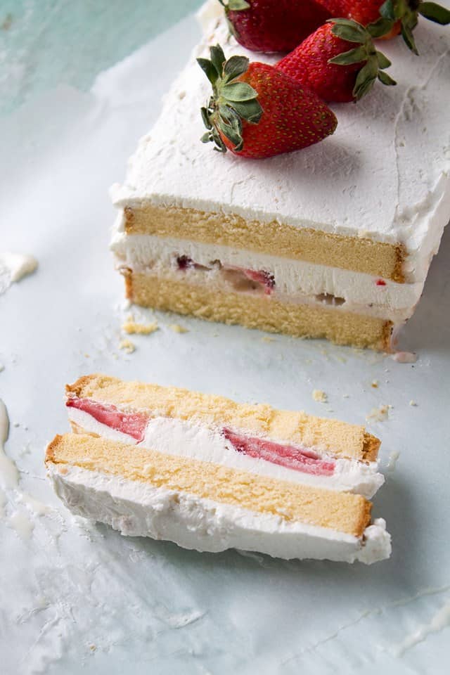 A single slice of Strawberries and Cream Ice Cream Cake lying on its side next to the rest of the cake.