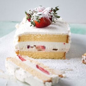 A frozen cake with a layer of strawberries and cream in the middle and whole strawberries on top.