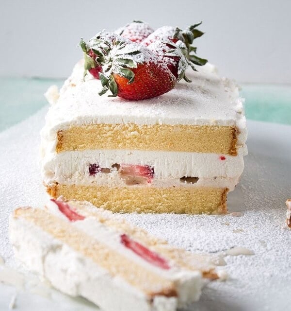 A frozen cake with a layer of strawberries and cream in the middle and whole strawberries on top.