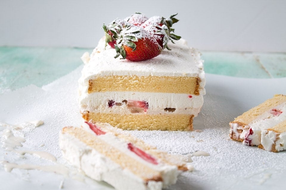 A frozen cake with a layer of strawberries and cream in the middle and whole strawberries on top.