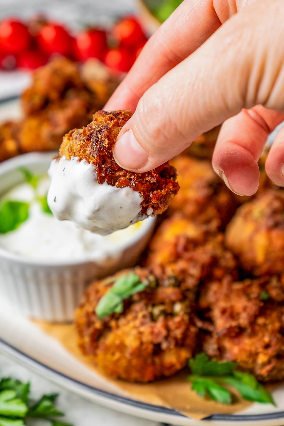 A hand holding up a veggie meatball with white sauce on the end of it.