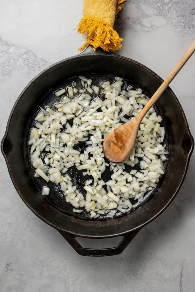 A skillet full of cooked onions, with a wooden spoon