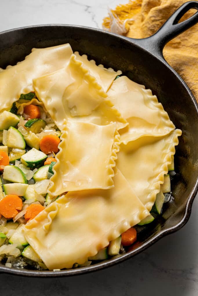 Some lasagna noodles covering a vegetable mixture in a skillet