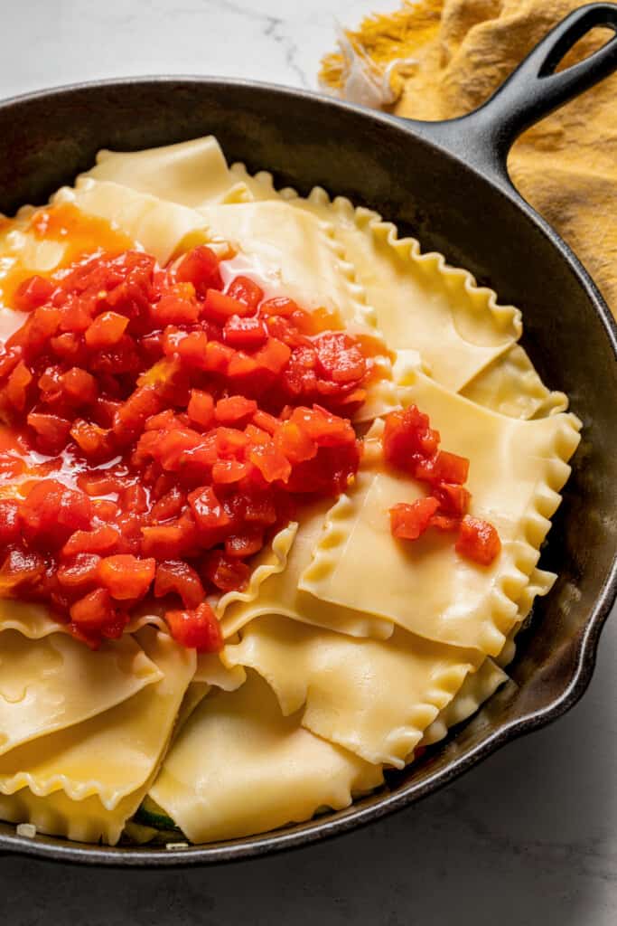 Some canned tomatoes on top of lasagna noodles in a skillet